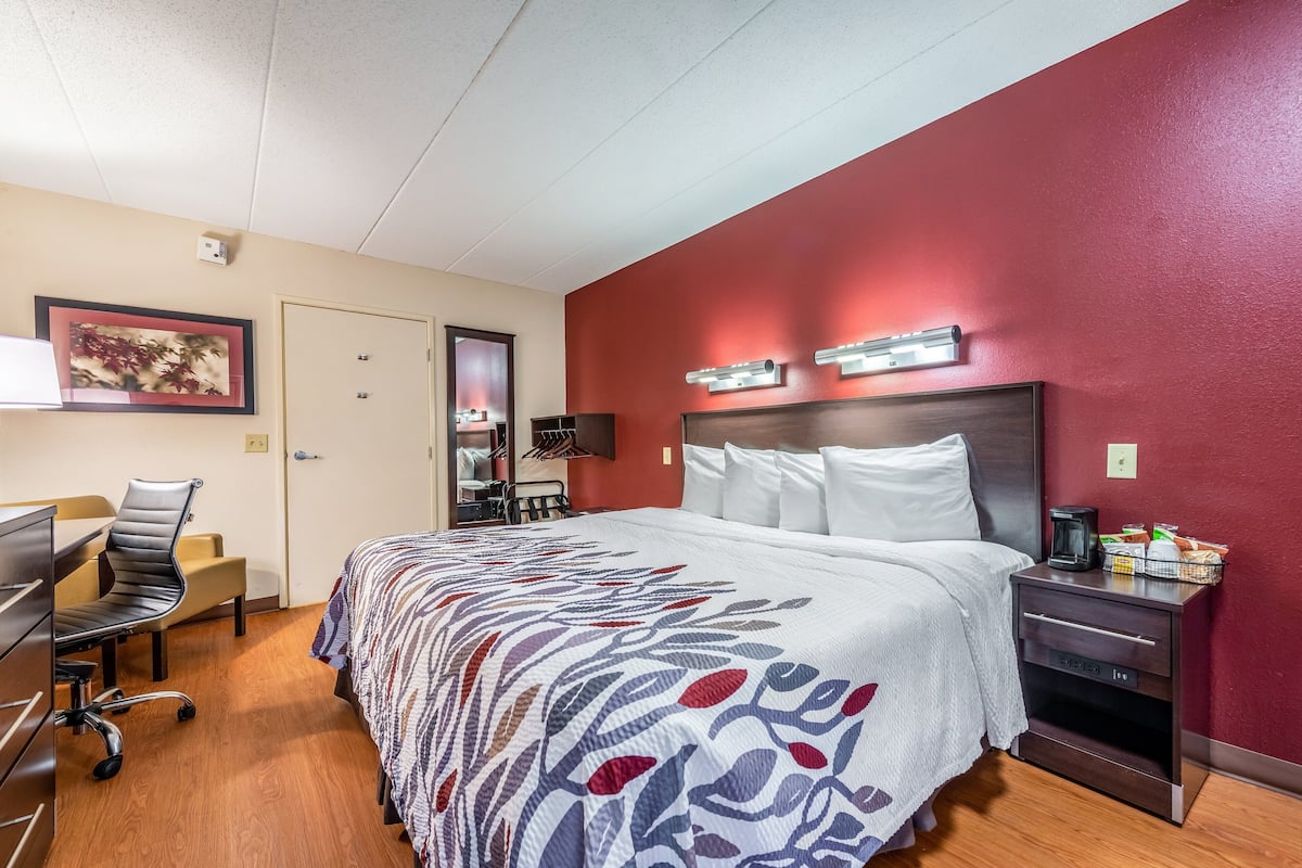 A hotel room with a large bed, a desk with a chair, a dresser, and a nightstand with a lamp.