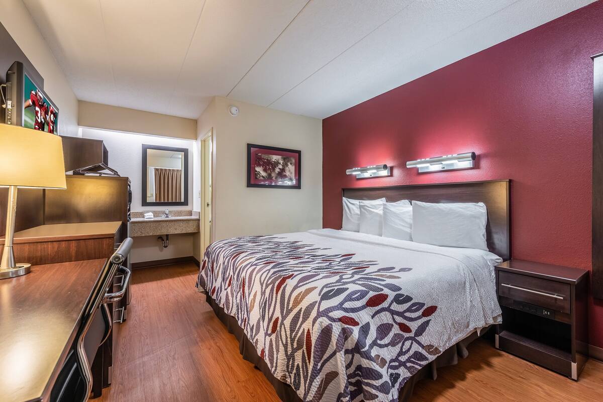 A hotel room with a bed, bedside table, lamp, and a desk with a chair.