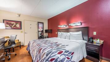Habitación de hotel con cama, mesita de noche, escritorio, silla y una pared decorada en rojo.