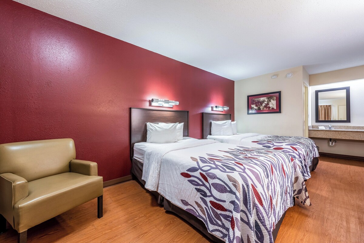 A hotel room with a bed, a chair, and a mirror.