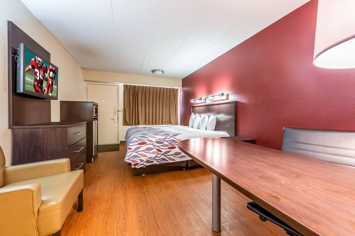 A hotel room with a bed, a desk, a chair, a TV, and a wardrobe.