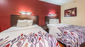 A hotel room with two beds, each with a headboard and pillows, a bedside table, and a wall-mounted light fixture. - Red Roof Inn Merrillville (Merrillville)