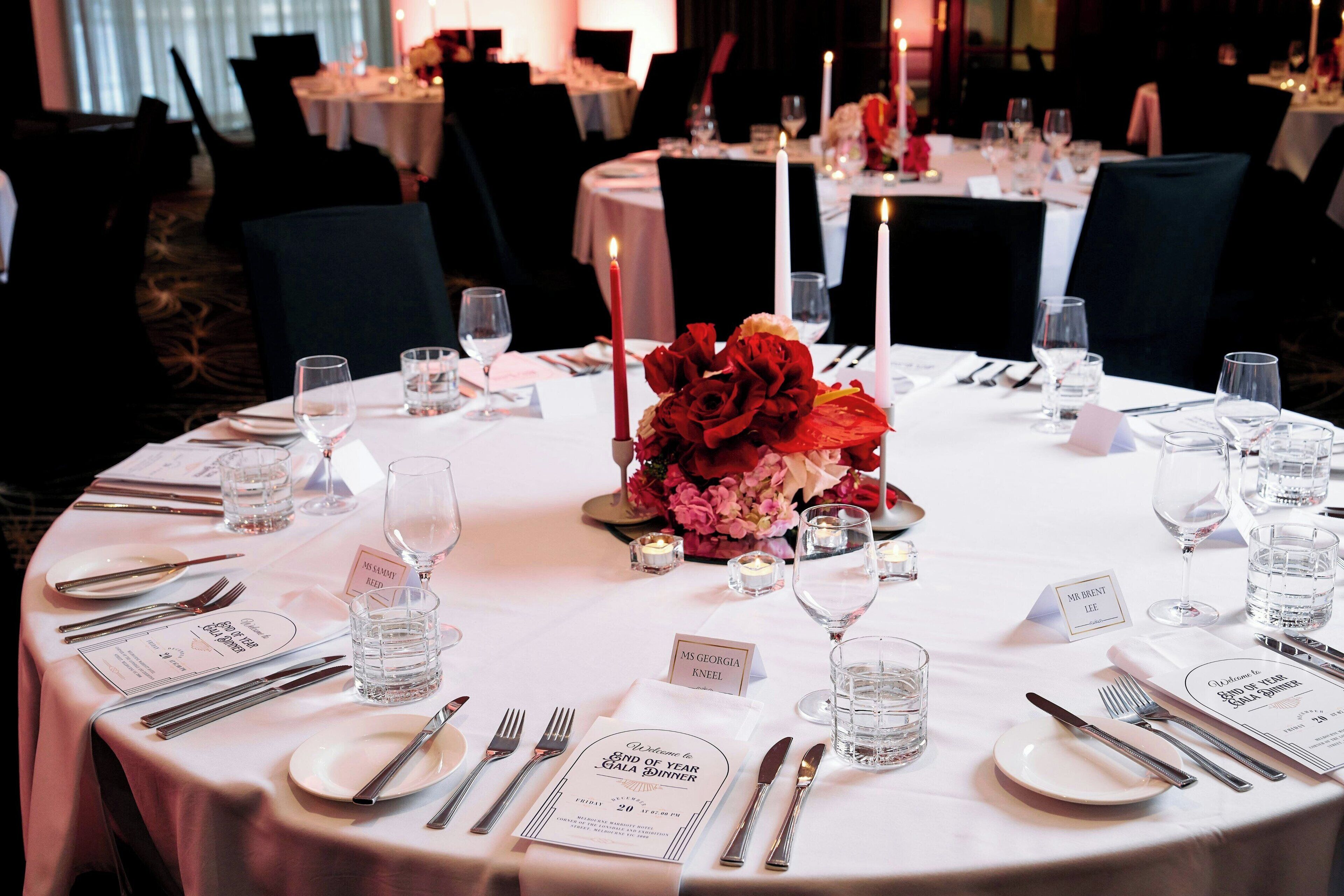 A round dining table set with white tablecloths, candles, and floral centerpieces.