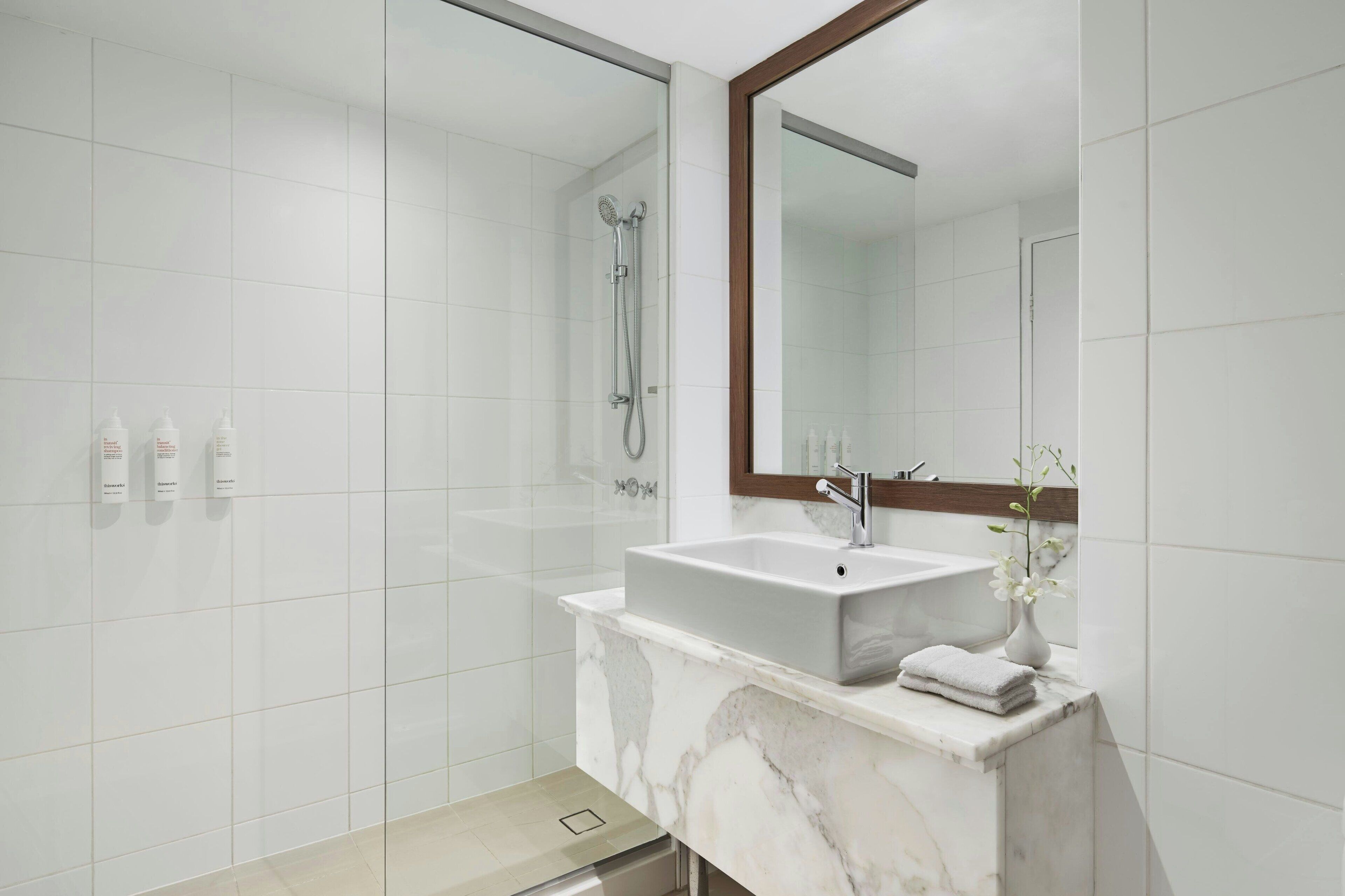 A modern bathroom with a large mirror, a marble sink, and a shower.
