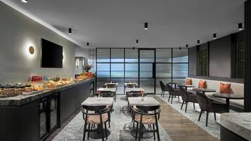 Un comedor moderno con bufé, mesas dispuestas y vistas amplias por ventanas grandes.