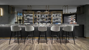 Una zona de bar moderna con una encimera de mármol, cuatro taburetes y una estantería bien surtida con diversas botellas.
