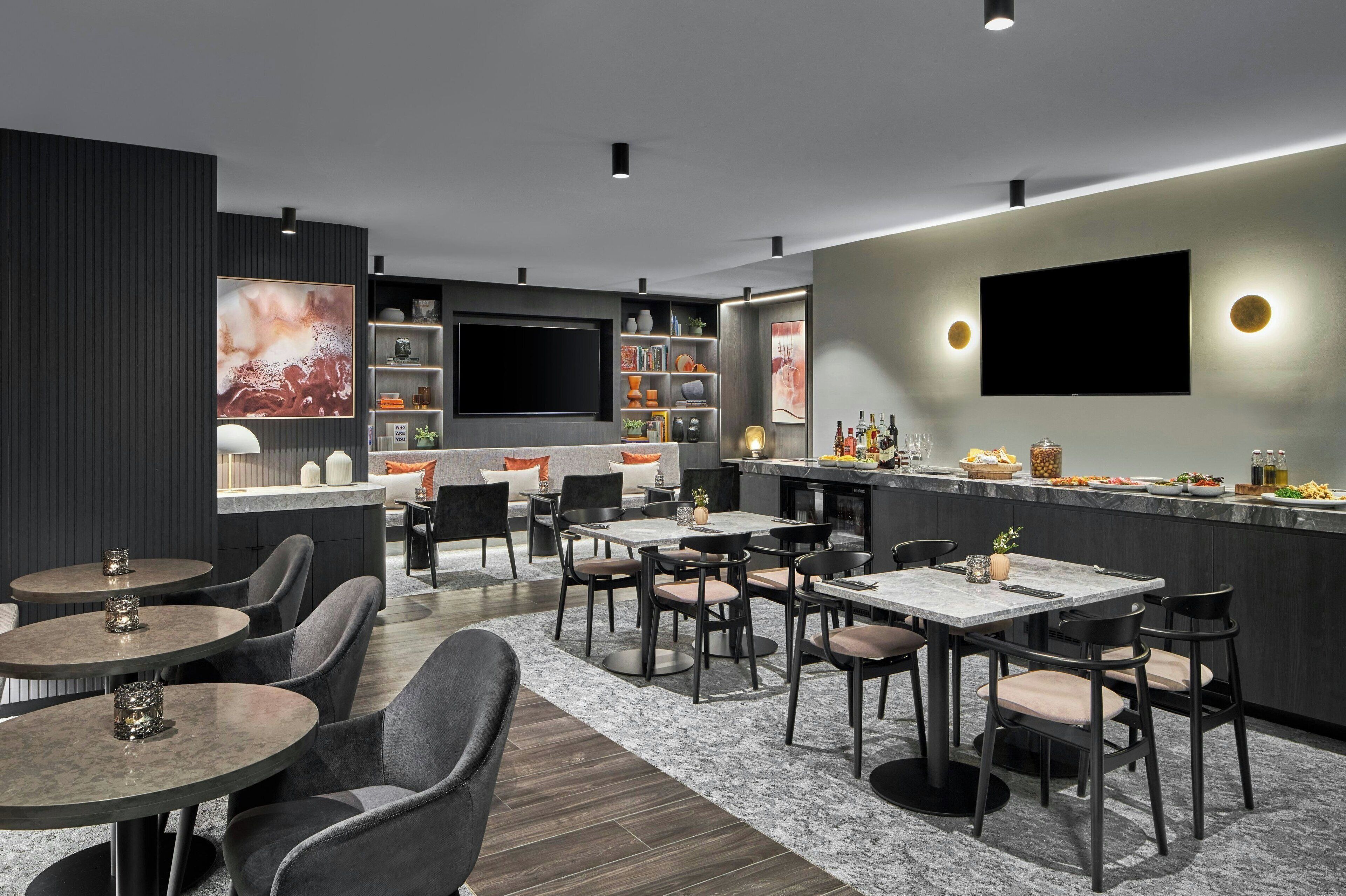 A modern bar area with seating, a TV, and a variety of bottles and glasses.