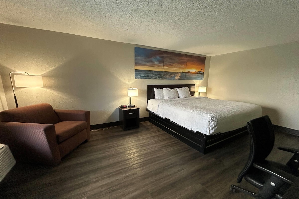 A hotel room with a bed, nightstands, a desk, a chair, a sofa, and a painting on the wall.