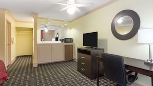 A hotel room with a ceiling fan, a desk with a chair, a TV, a microwave, and a small kitchenette with a sink and cabinets. - Days Inn by Wyndham Savannah Airport (Garden City)