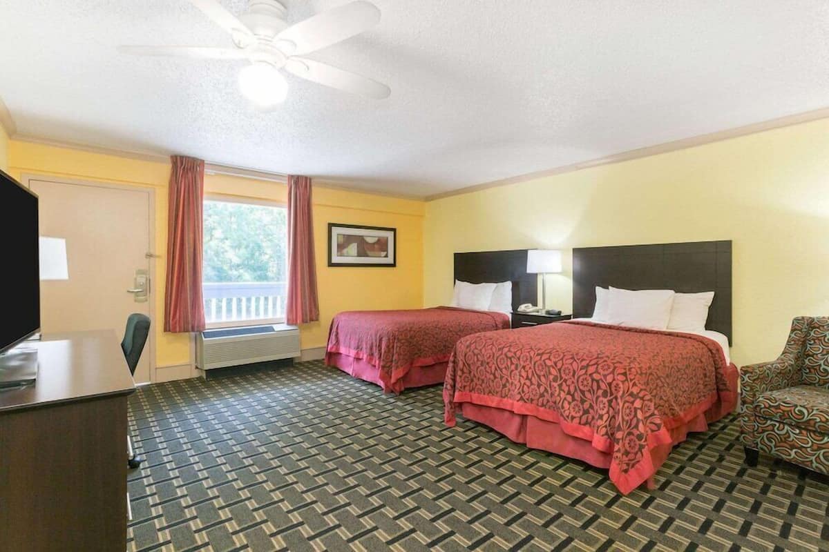 A hotel room with two beds, a desk, a chair, a ceiling fan, and a window with curtains.
