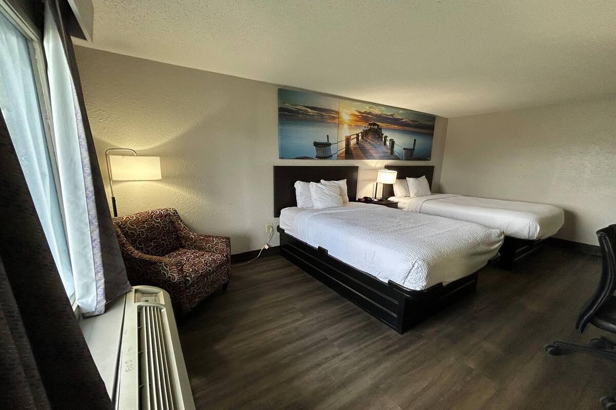 A hotel room with a bed, two bedside tables, a lamp, a chair, and a painting on the wall.