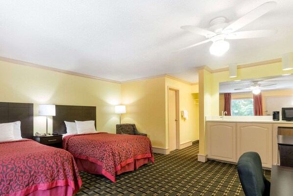 Une chambre d’hôtel avec deux lits, un bureau, une chaise, une kitchenette et un ventilateur de plafond.