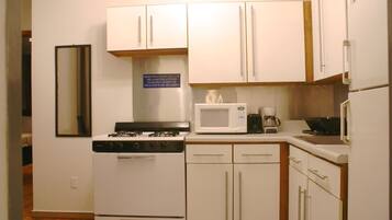 A compact kitchen with white cabinets, a stove, a microwave, and a coffee maker.