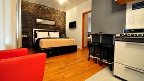A bedroom with a bed, a TV, a red chair, and a kitchen area with a stove. - Off Soho Suites Hotel (New York)