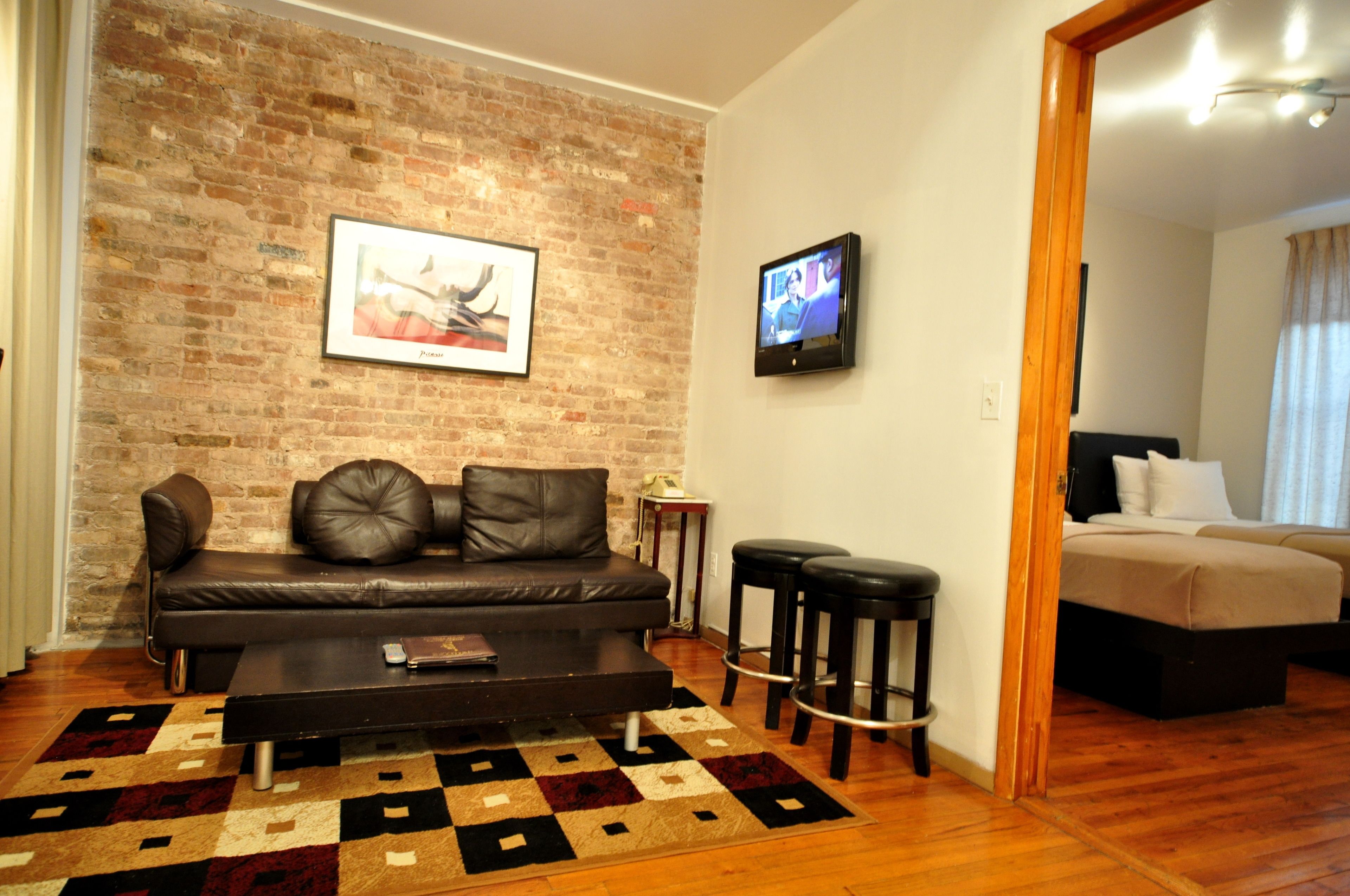 Una sala de estar con pared de ladrillo, sofá de cuero, mesa de centro y televisor en la pared.