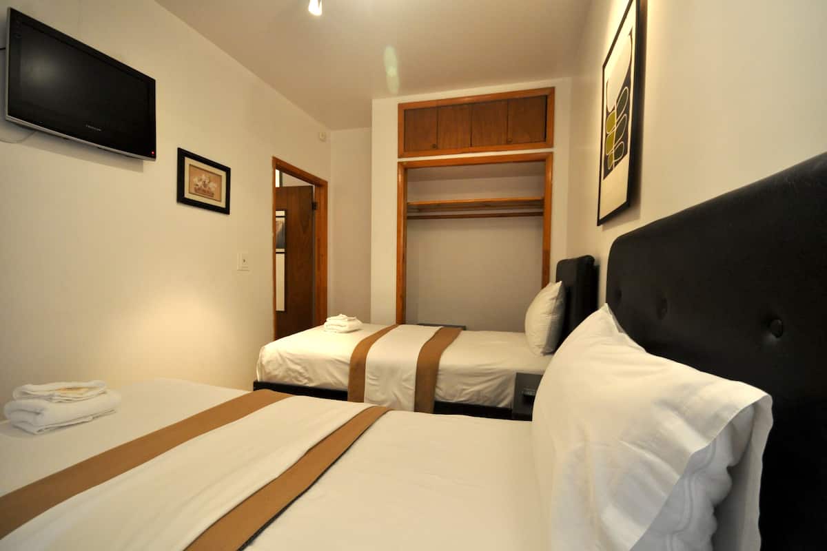 A hotel room with two beds, a television, a wardrobe, and a framed picture on the wall.