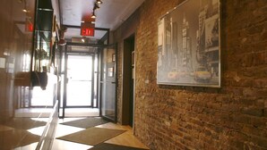 A hallway with a brick wall, a framed cityscape picture, and a glass door leading to a bright area. - Off Soho Suites Hotel (New York)