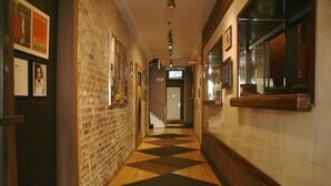 A hallway with a brick wall, wooden floor, and a staircase leading to an elevator. - Off Soho Suites Hotel (New York)