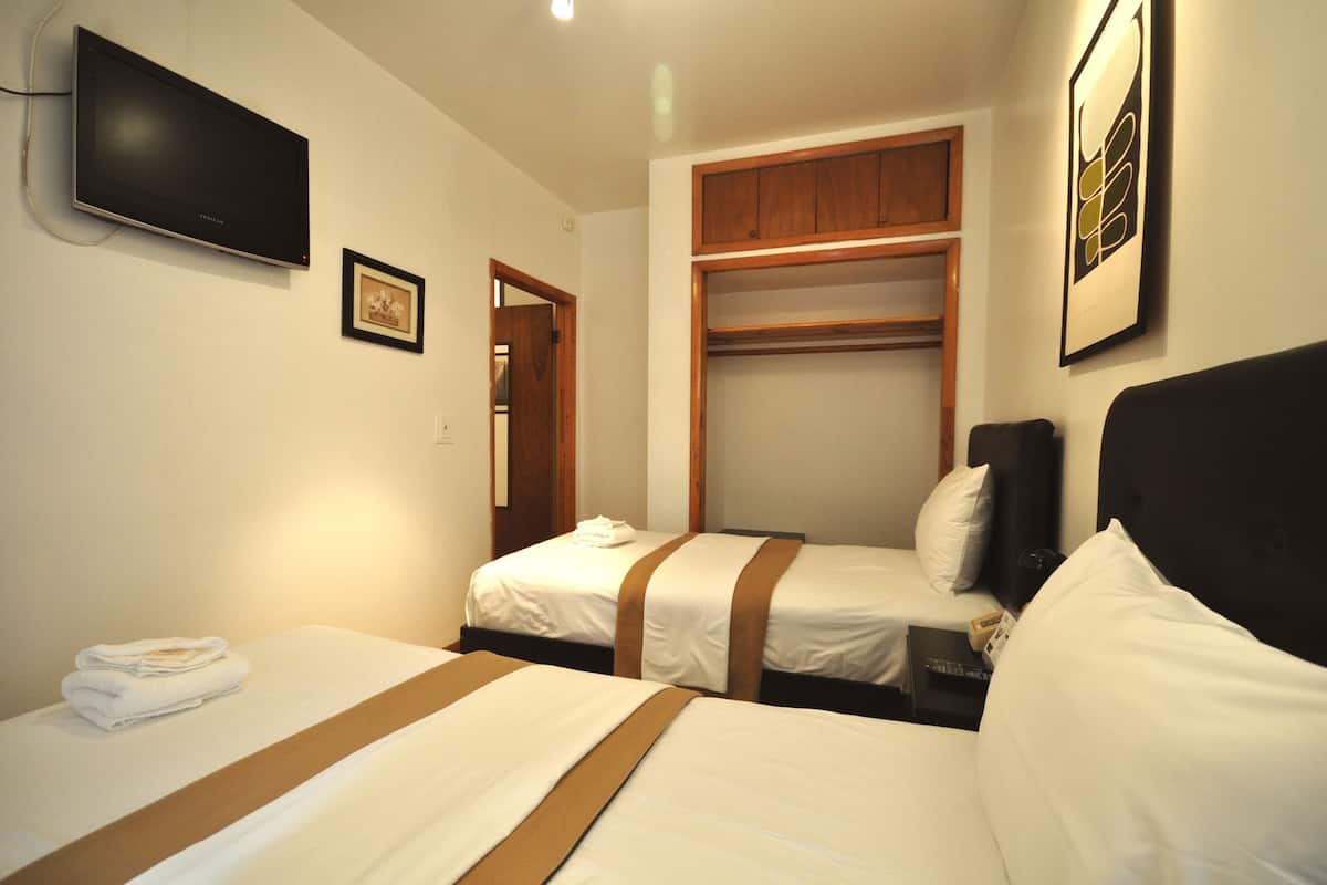 A hotel room with two beds, a TV mounted on the wall, a wooden closet, and a framed picture on the wall.