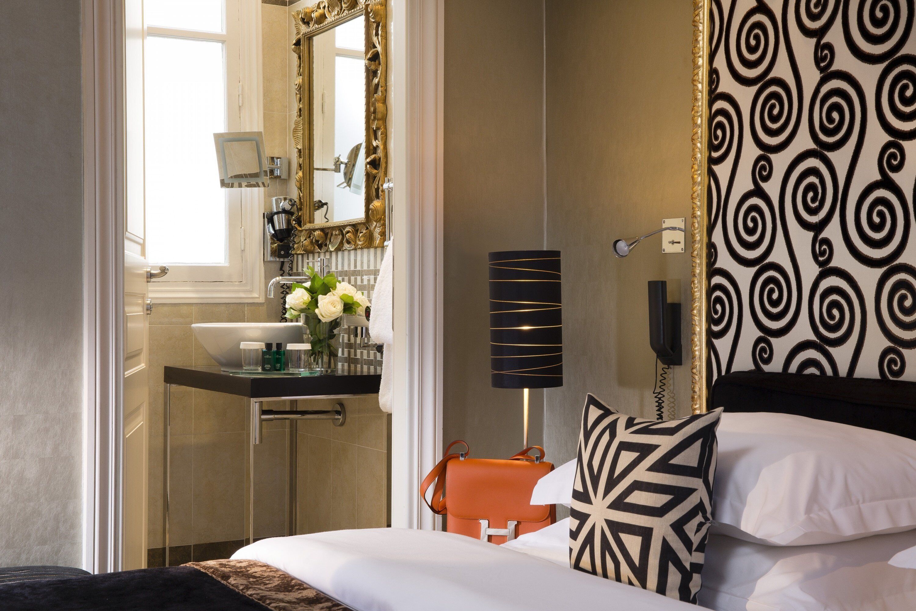 A hotel room with a bed, a bathroom with a sink and mirror, and a patterned wall.