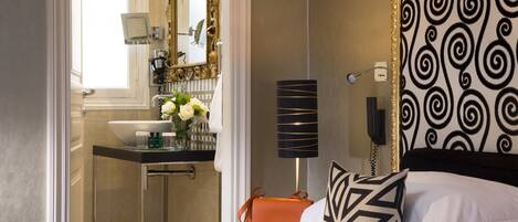 A hotel room with a bed, a bathroom with a sink and mirror, and a patterned wall.