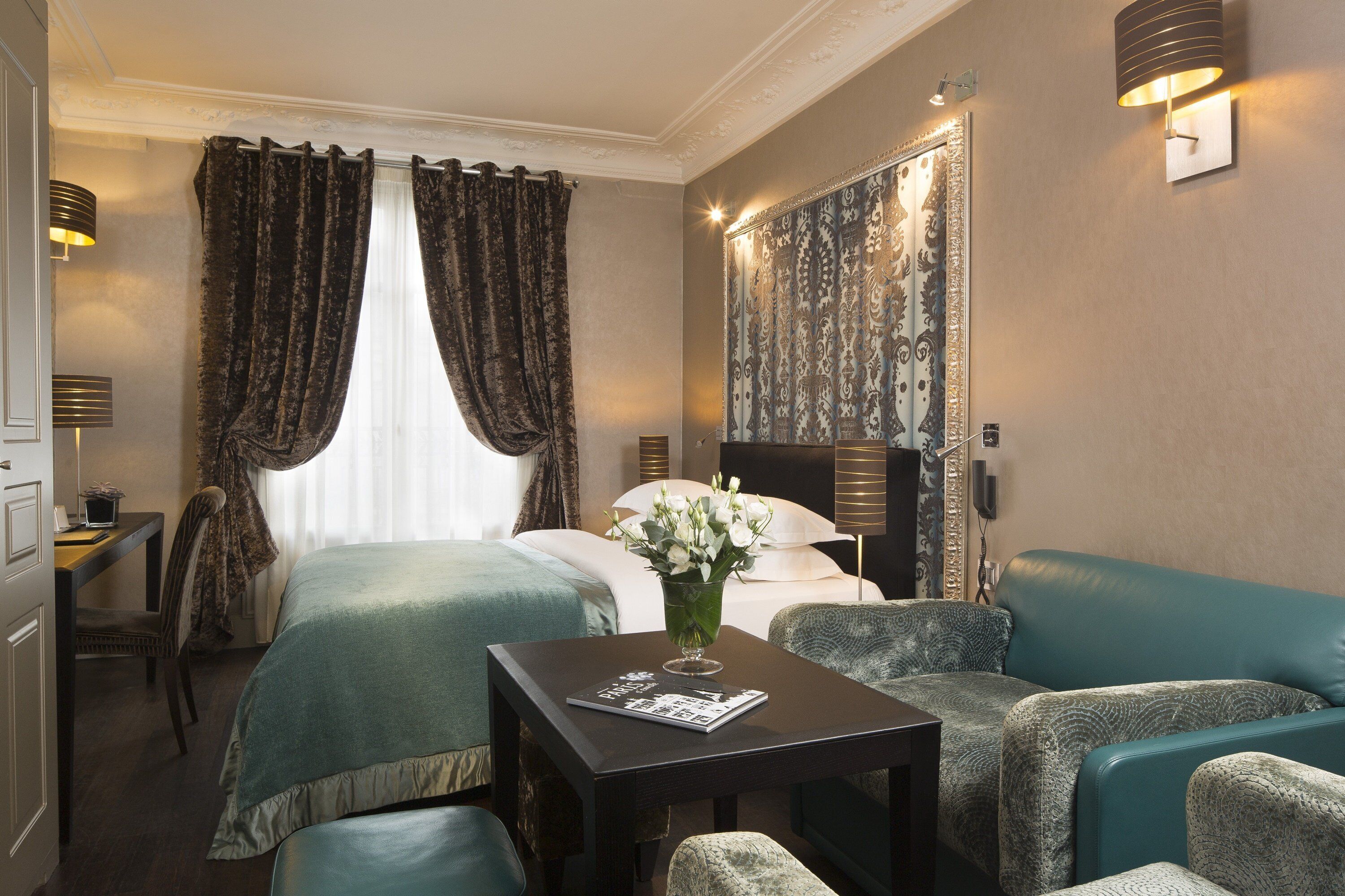 A hotel room with a bed, a desk, a chair, a sofa, and a table with a vase of flowers.