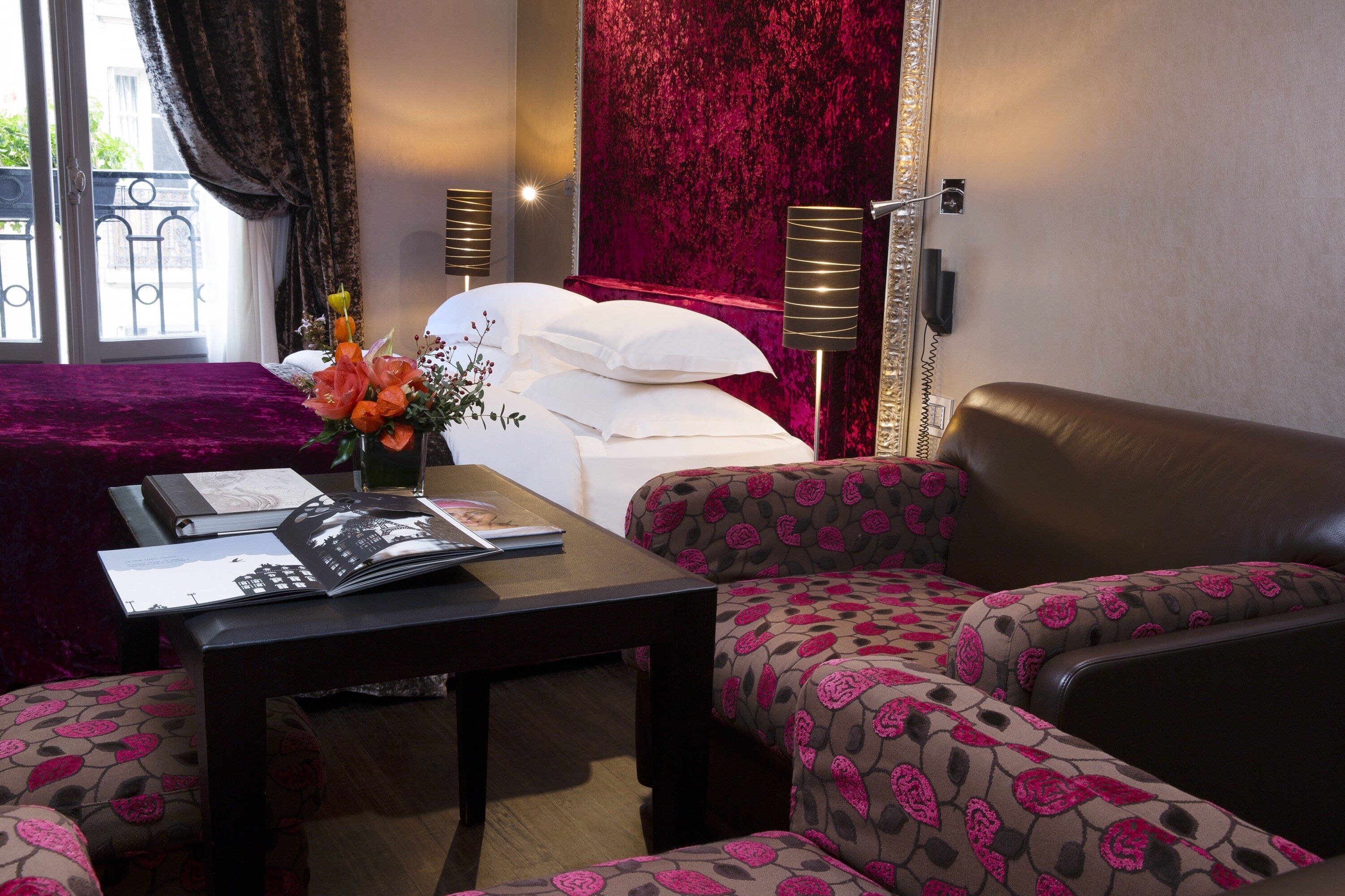 A hotel room with a bed, a sofa, a table with a magazine, and a vase with flowers.