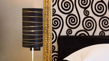A room with a black and white patterned wallpaper, a black lamp with gold stripes, and a gold-framed mirror.