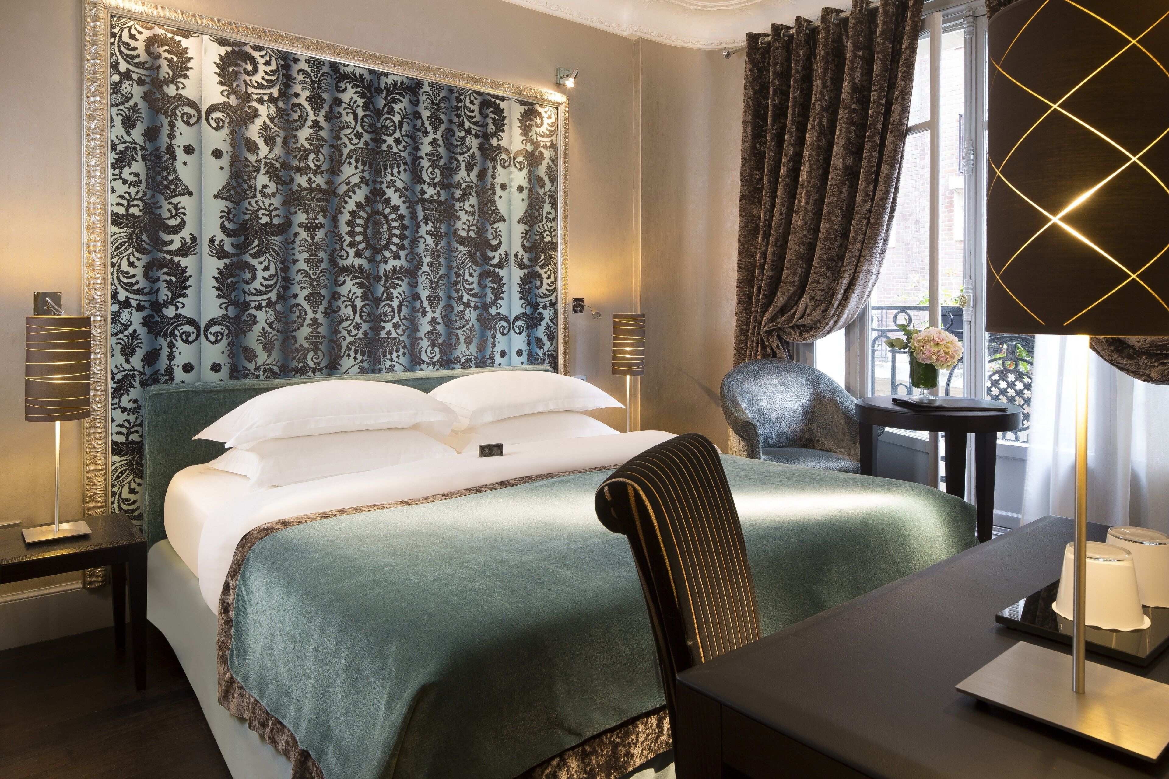 A hotel room with a large bed, a chair, a small table, and a lamp.