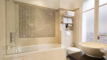 A modern bathroom with a glass-enclosed shower, a freestanding bathtub, a vanity with a large vessel sink, and a towel rack with neatly folded towels.