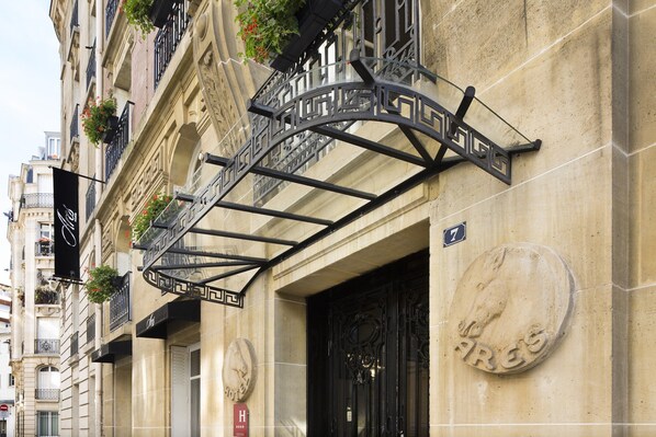 Experience the charm of this historic building with ornate ironwork and a detailed facade, featuring a large stone entrance plaque and multiple balconies with flower boxes.
