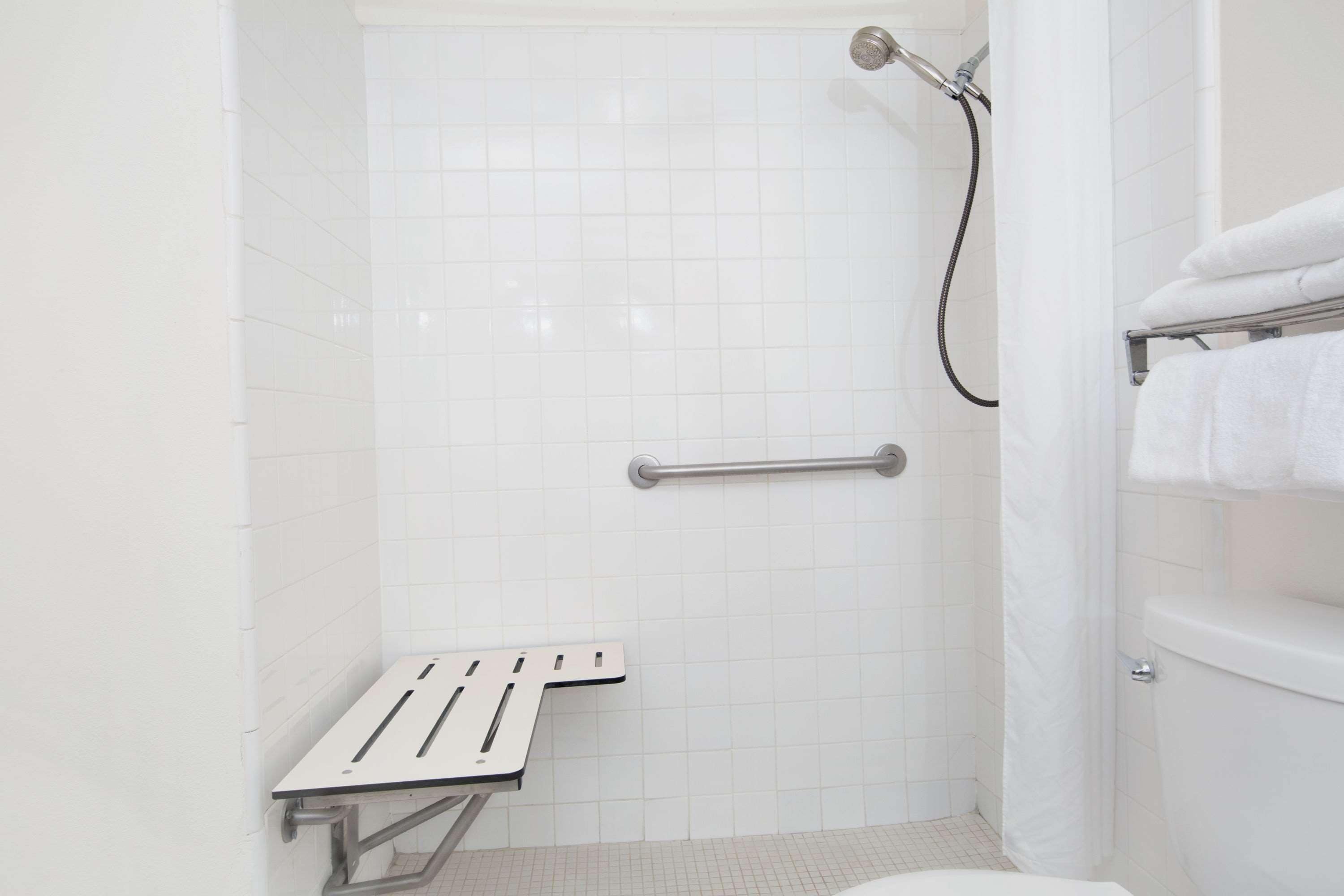 Un baño moderno con azulejos blancos, una ducha con cabezal de ducha manual, una barra de apoyo y un perchero.