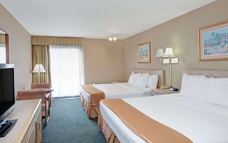 A hotel room with two beds, a desk with a TV, a lamp, and a painting on the wall.