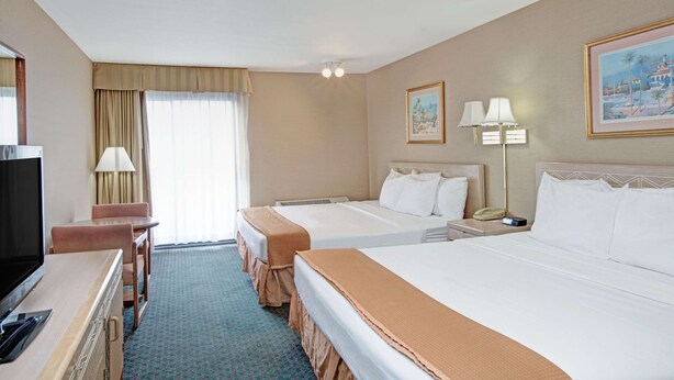 A hotel room with two beds, a desk with a TV, a lamp, and a painting on the wall. - Howard Johnson by Wyndham Torrance (Torrance)