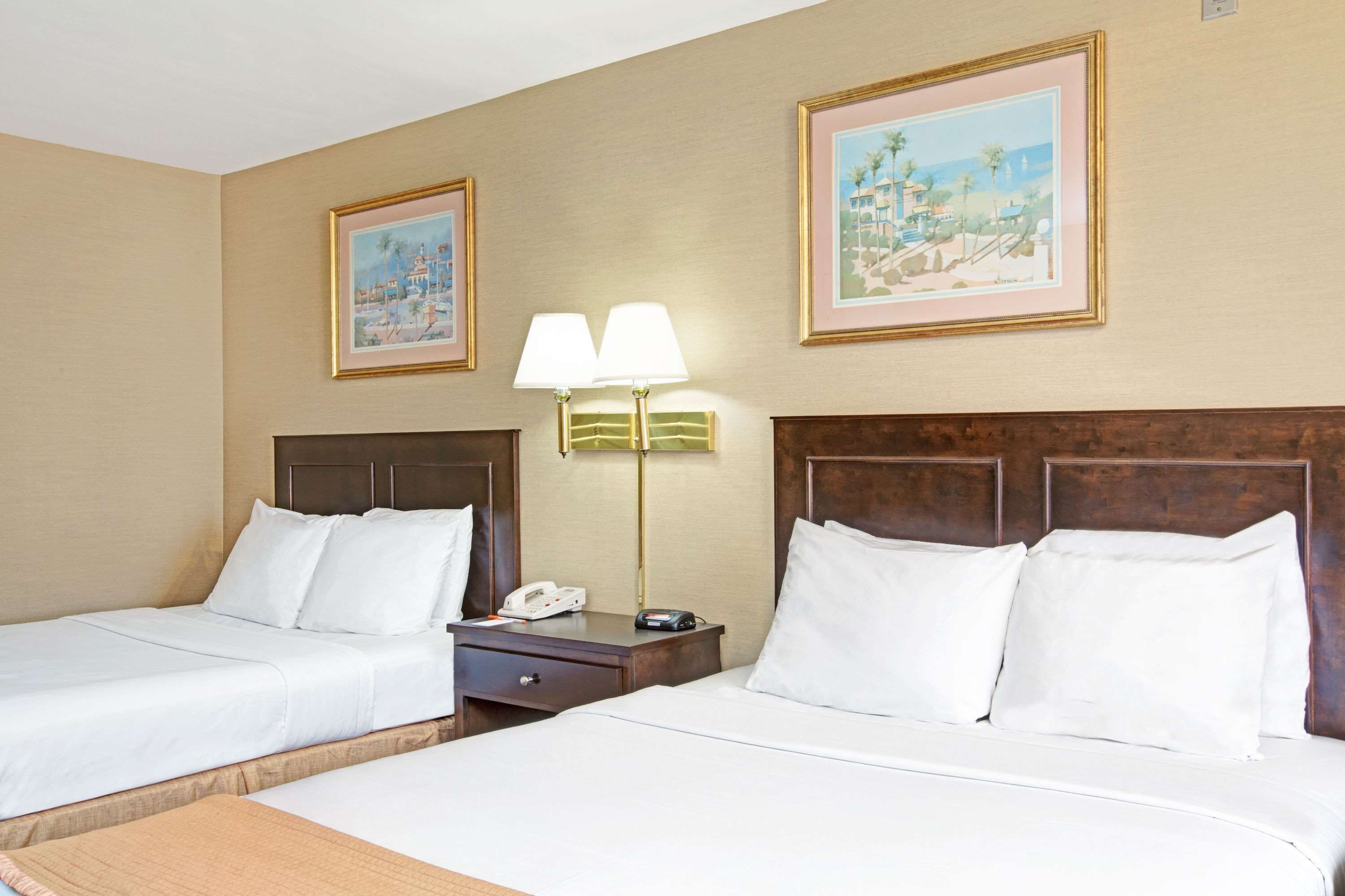 A hotel room with two beds, a nightstand, a lamp, and two framed pictures on the wall.