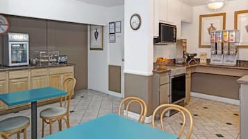 Una cocina con cafetera, tostadora y dispensador de cereales. Hay sillas y una mesa.