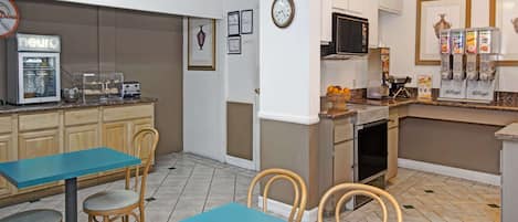 Una cocina con cafetera, tostadora y dispensador de cereales. Hay sillas y una mesa.