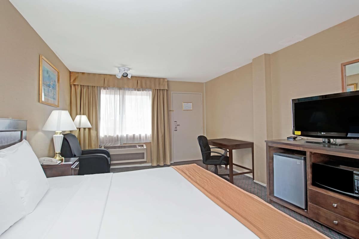 Hotellihuone, jossa on suuri sänky, työpöytä, jossa on televisio, pieni jääkaappi ja tuoli.