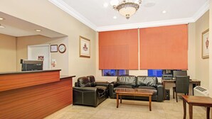 A reception area with a wooden desk, black leather sofas, a wooden coffee table, and a large window with blinds. - Howard Johnson by Wyndham Torrance (Torrance)