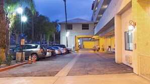 A hotel entrance with a covered walkway, parked cars, and a palm tree. - Howard Johnson by Wyndham Torrance (Torrance)
