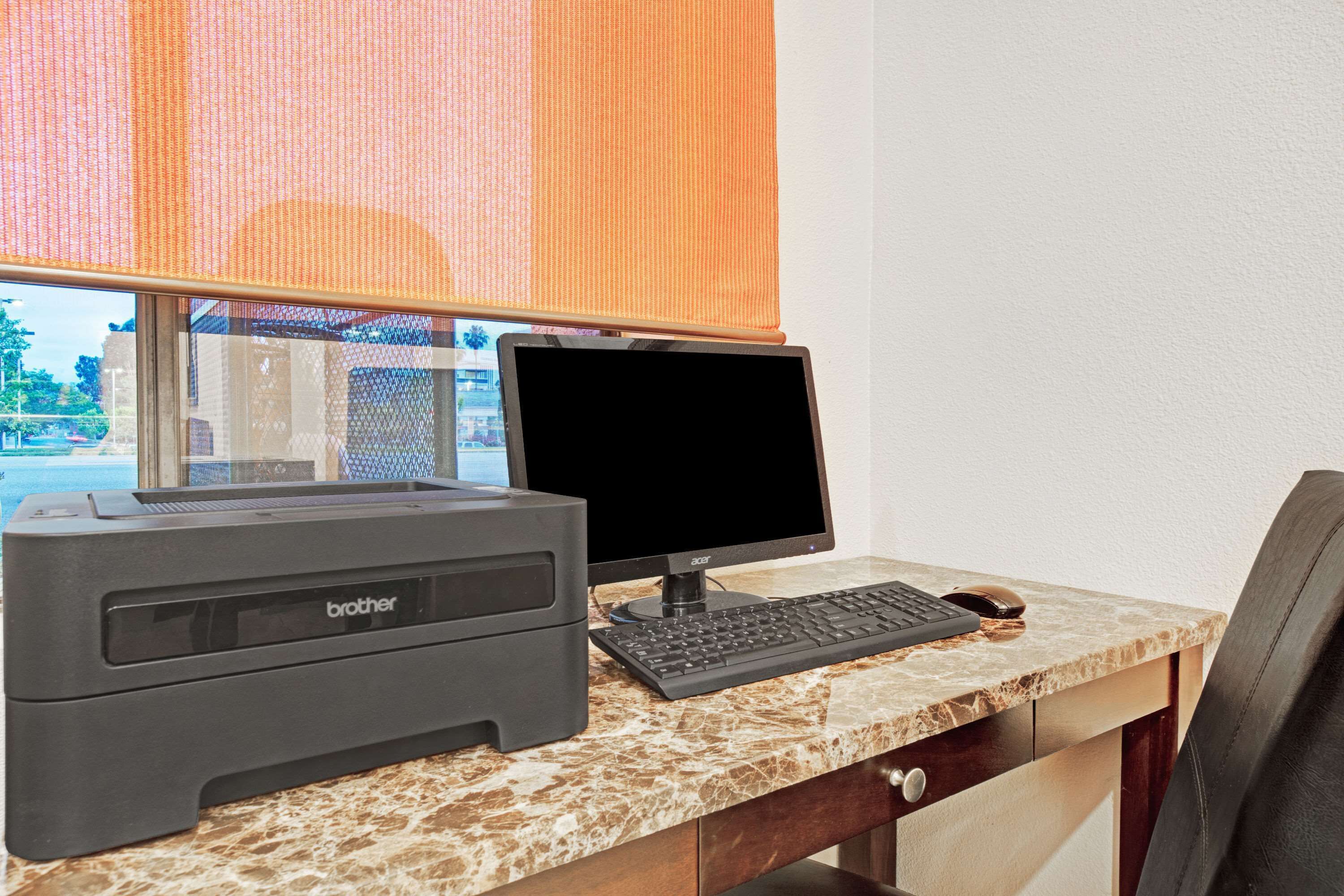 A Brother printer and monitor on a marble desk with a window view.
