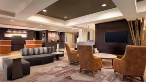 A modern lounge area with a sofa, chairs, a coffee table, and a flat-screen TV. - Courtyard Bloomington Normal (Normal)