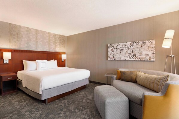 Una habitación de hotel con una cama grande, un sofá, una mesita de noche y una lámpara de pared.