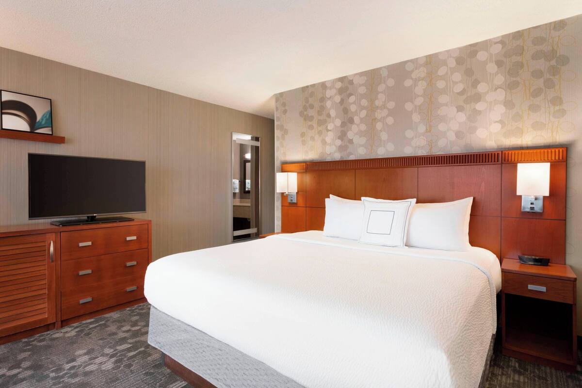 A hotel room with a large bed, a TV on a wooden dresser, and a patterned wall.
