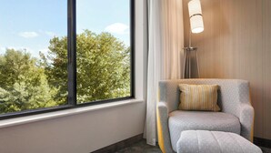 A room with a large window, a grey armchair with a striped pillow, and a floor lamp. - Courtyard Bloomington Normal (Normal)