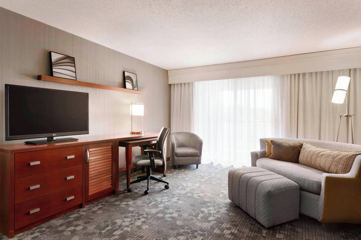 A hotel room with a flat-screen TV, a desk, a comfortable sofa, and a chair.