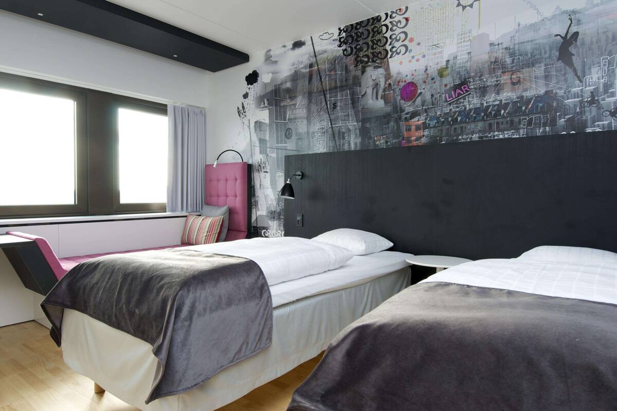 A modern hotel room with two beds, a desk, and a large window.