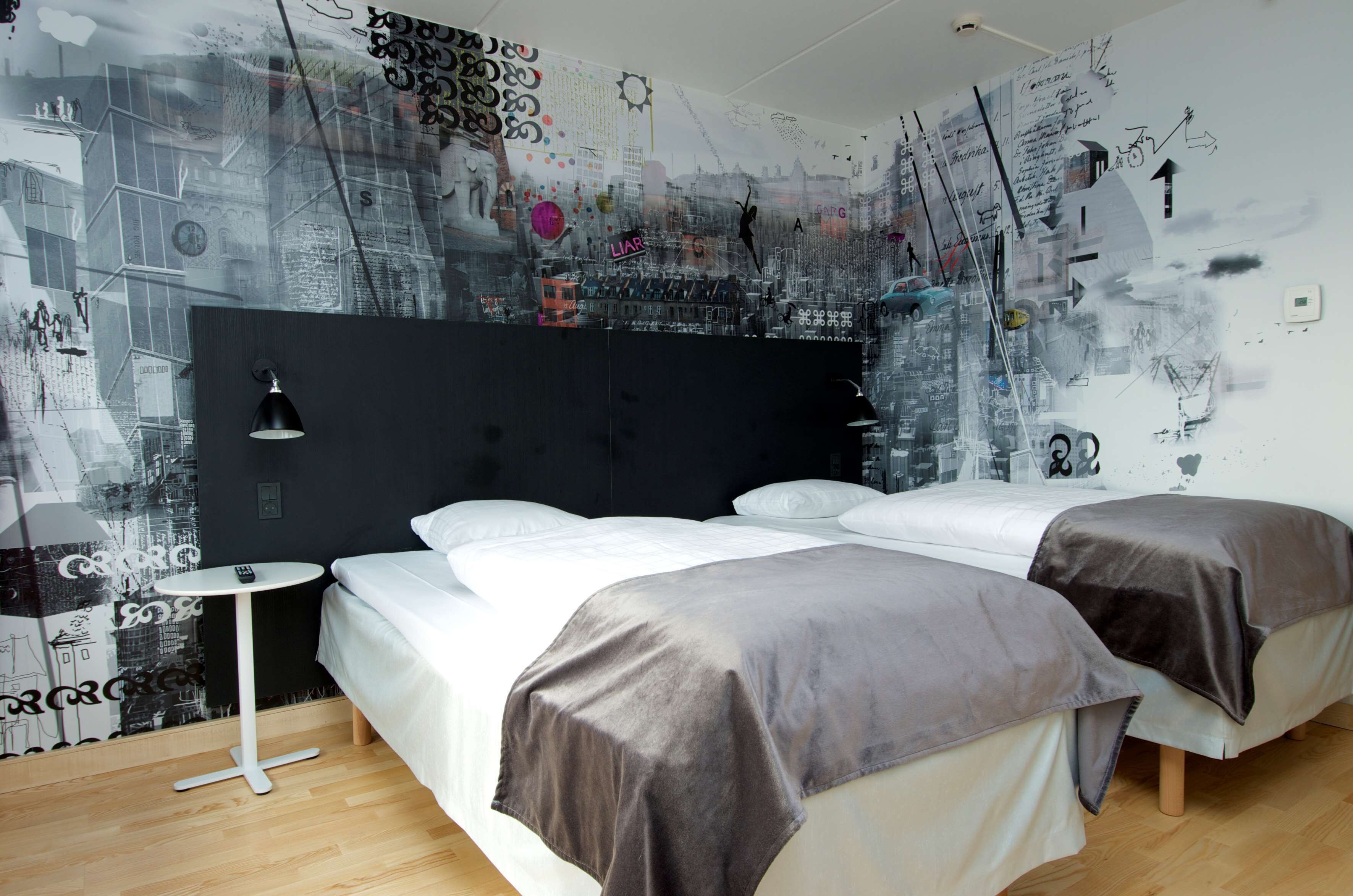 A modern hotel room with a large bed, two bedside tables, a black headboard, and a wall with artistic graffiti-style designs.