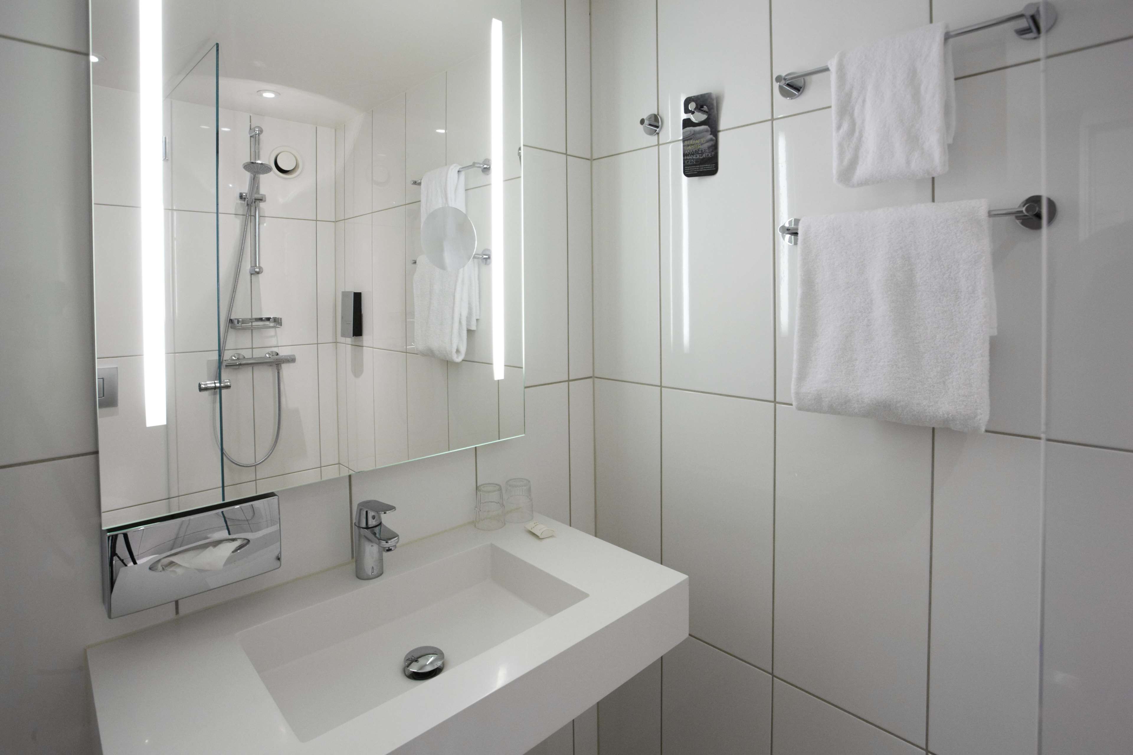 Un baño moderno con un lavamanos blanco, cabina de ducha con vidrio y un espejo grande.