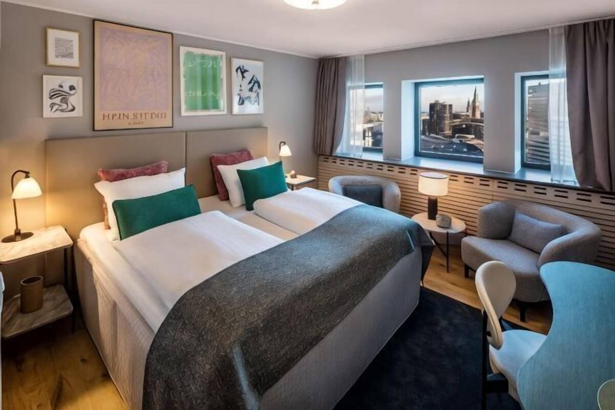 A hotel room with two beds, a sofa, a chair, a desk, and a window with a city view.